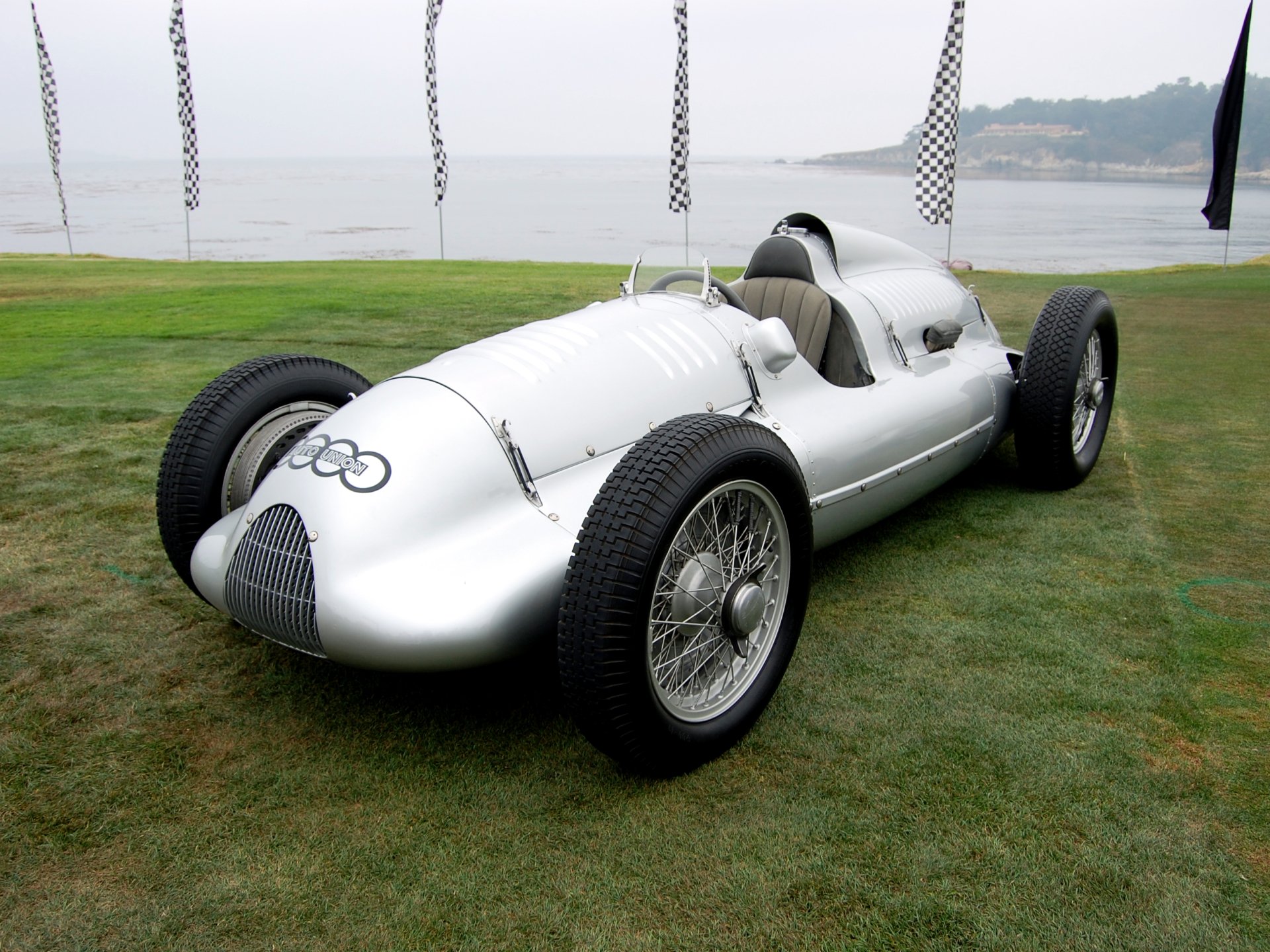HD desktop wallpaper featuring a sleek silver 1939 Audi D-Type race car parked on grass near a waterfront.