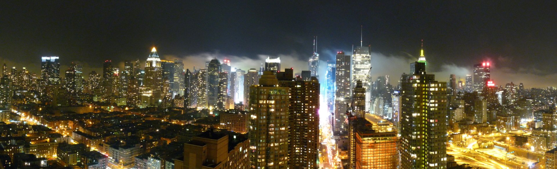 HD desktop wallpaper showing a vibrant nighttime cityscape of New York with illuminated skyscrapers and glowing streets under a misty sky.