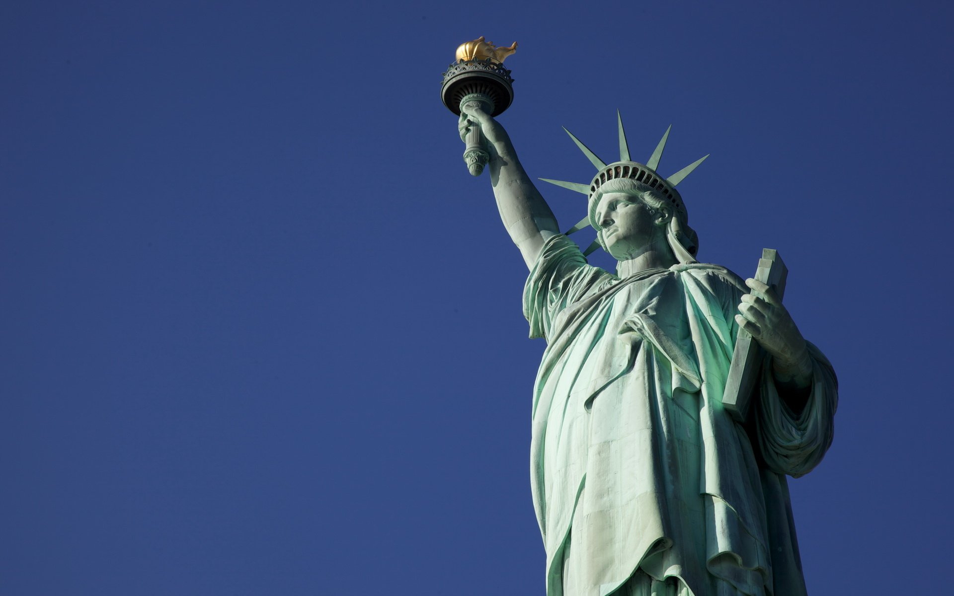 HD desktop wallpaper featuring a close-up of the man-made Statue of Liberty against a clear blue sky.