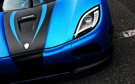 Close-up of a blue and black Koenigsegg Agera R, focusing on the headlight and the front hood with a sleek design. Image can be used as HD desktop wallpaper and background.