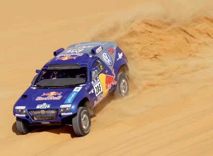 Blue Volkswagen Touareg rally vehicle kicking up sand across desert dunes — 2K Quad HD PC desktop wallpaper and background.