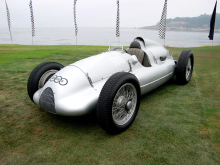 HD desktop wallpaper featuring a sleek silver 1939 Audi D-Type race car parked on grass near a waterfront.