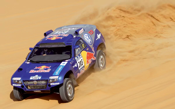 Blue Volkswagen Touareg rally vehicle kicking up sand across desert dunes — 2K Quad HD PC desktop wallpaper and background.