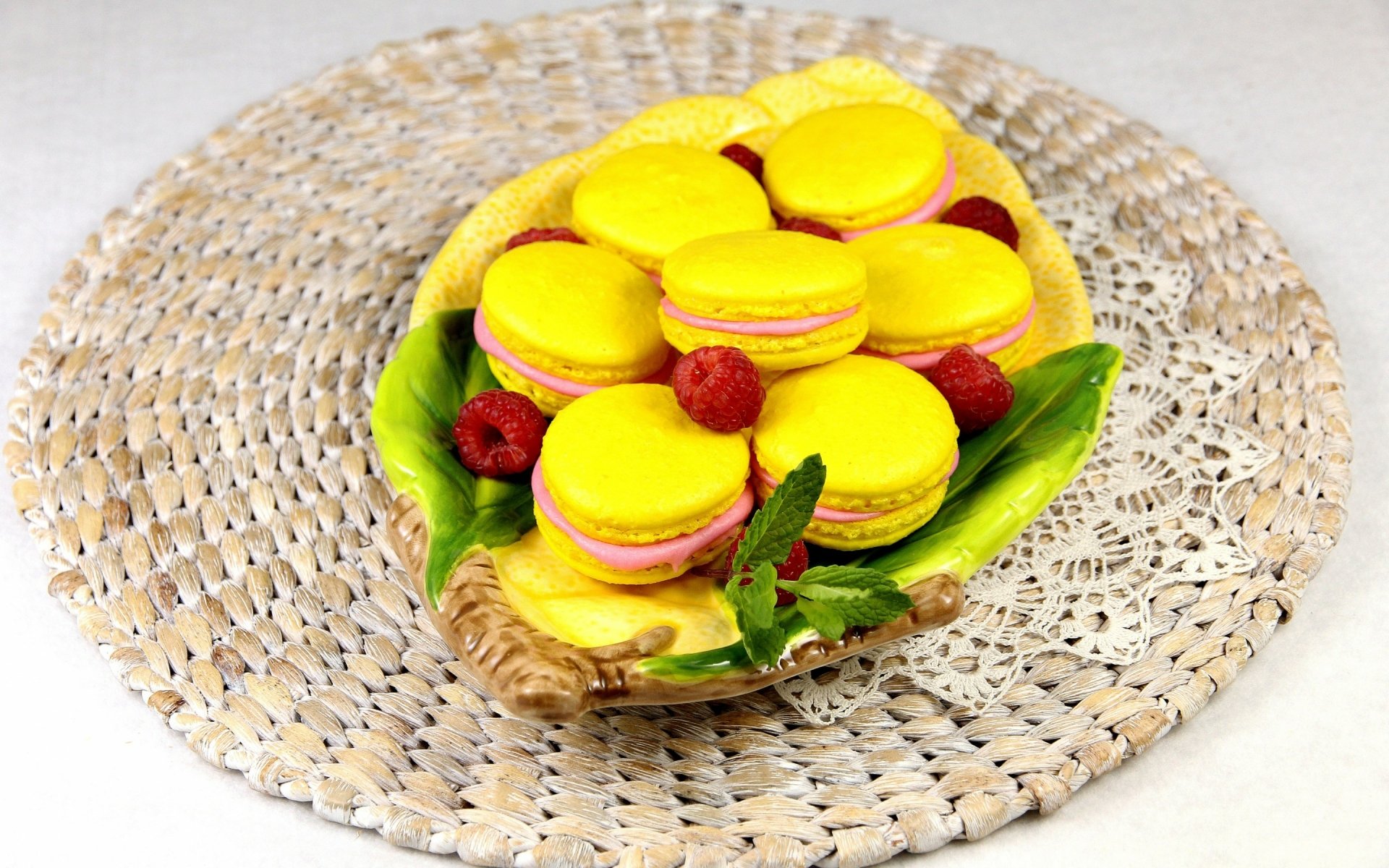 HD desktop wallpaper featuring a close-up of yellow macarons with raspberries and mint leaves on a decorative woven placemat.