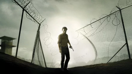 HD wallpaper of Andrew Lincoln as Rick Grimes from the TV show The Walking Dead, standing by a barbed wire fence under a gloomy sky.