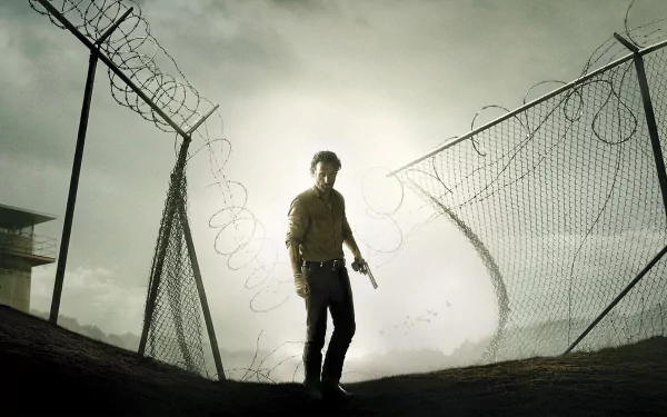 HD wallpaper of Andrew Lincoln as Rick Grimes from the TV show The Walking Dead, standing by a barbed wire fence under a gloomy sky.
