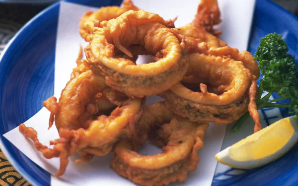 HD desktop wallpaper featuring a close-up of golden-brown grilled octopus rings served with lemon and parsley, highlighting seafood cuisine and octopus food.