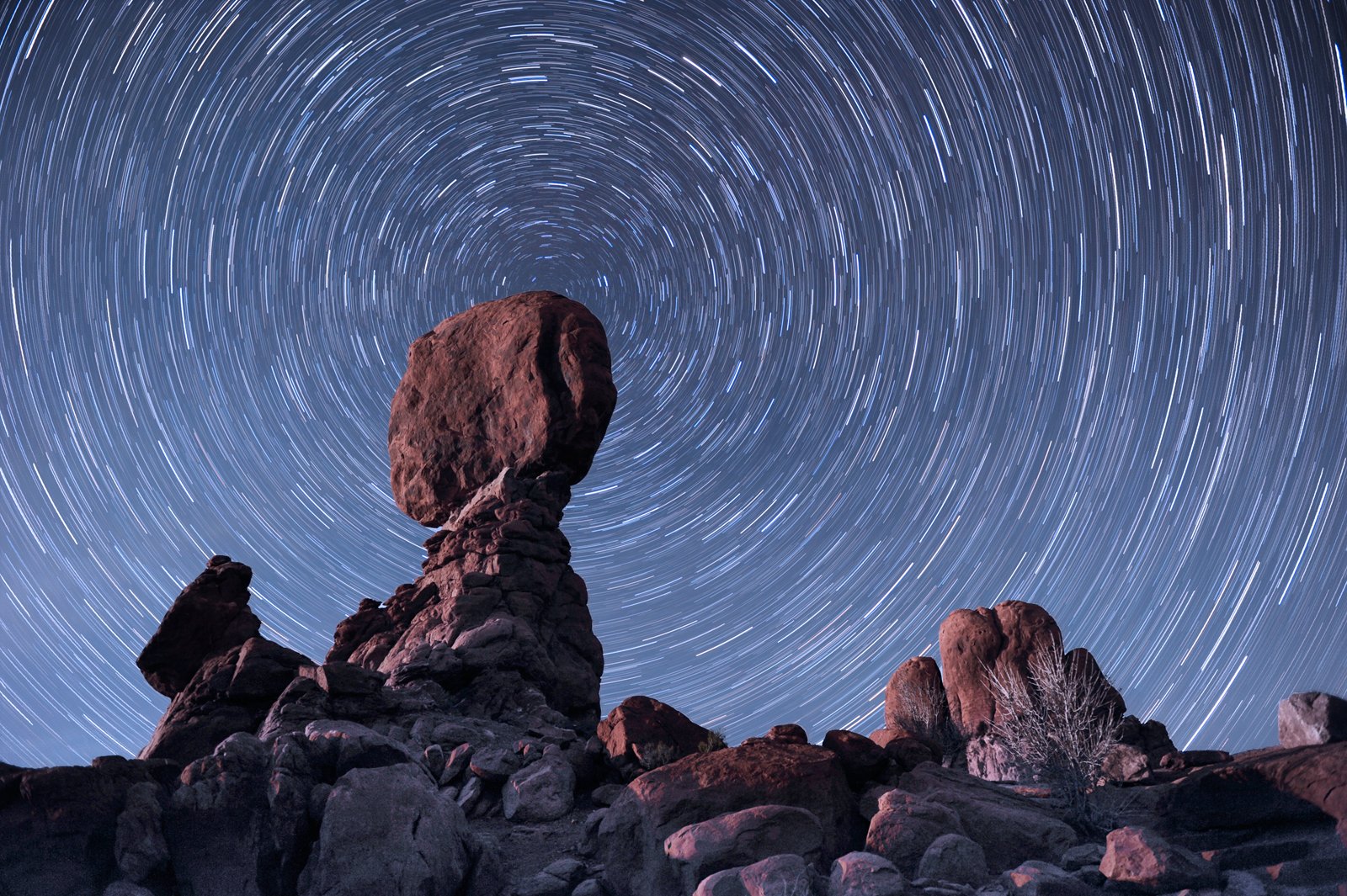 HD PC desktop wallpaper showing a natural rock formation beneath swirling star trails in the night sky, highlighting the beauty of nature and celestial motion.