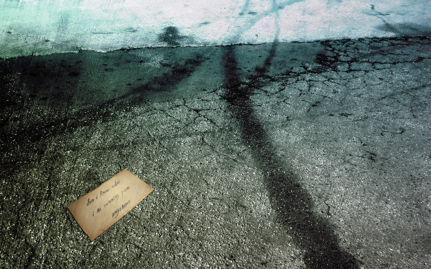Artistic HD PC desktop wallpaper featuring a cracked asphalt surface with a shadowy tree silhouette and a worn, handwritten note on the ground.