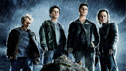 Four young men in dark jackets stand on rocky ground in pouring rain, brooding and powerful — HD PC desktop wallpaper from the movie The Covenant (2006).