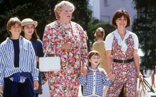 A vibrant HD wallpaper from the movie Mrs. Doubtfire, featuring a cheerful Robin Williams in disguise, surrounded by a group of children and an adult woman, capturing a lighthearted moment.