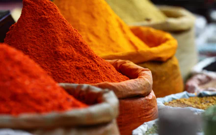 Vibrant piles of spices in warm hues, displayed in cloth sacks, create a rich tapestry of colors. A stunning HD desktop wallpaper celebrating food, herbs, and spices.