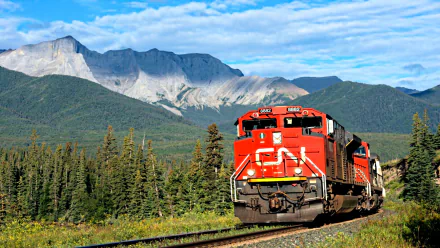 HD desktop wallpaper featuring a vibrant red train moving through a lush forest with towering mountains and a bright blue sky in the background.