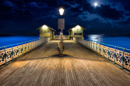 Man-made pier illuminated at night under a cloudy sky, captured in high definition as a PC desktop wallpaper and background.