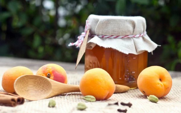 A 4K Ultra HD PC desktop wallpaper featuring fresh peaches, a jar of peach jam, wooden spoons, and spices on a natural fabric background.