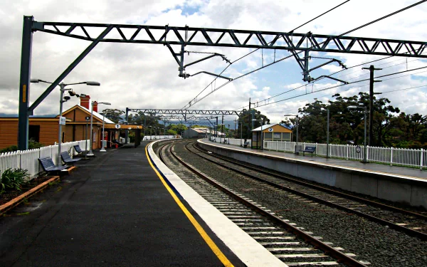 HD desktop wallpaper and background featuring an empty train station with tracks curving into the distance, overhead power lines, and buildings on either side.