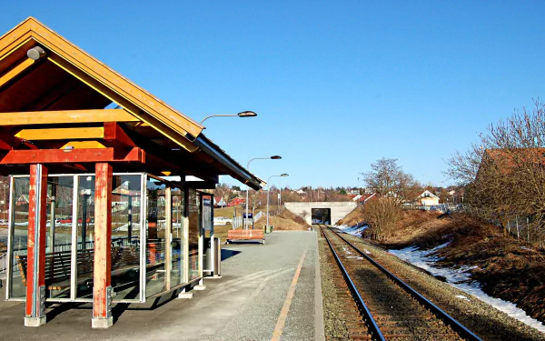 HD desktop wallpaper and background image featuring a quiet train station with a sheltered waiting area, tracks leading into the distance, and clear blue skies.