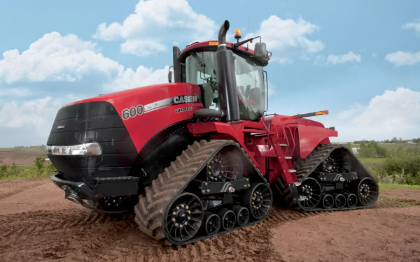 4K Ultra HD image of a red Case Quadtrac tractor with four track wheels on a dirt field under a partly cloudy sky.