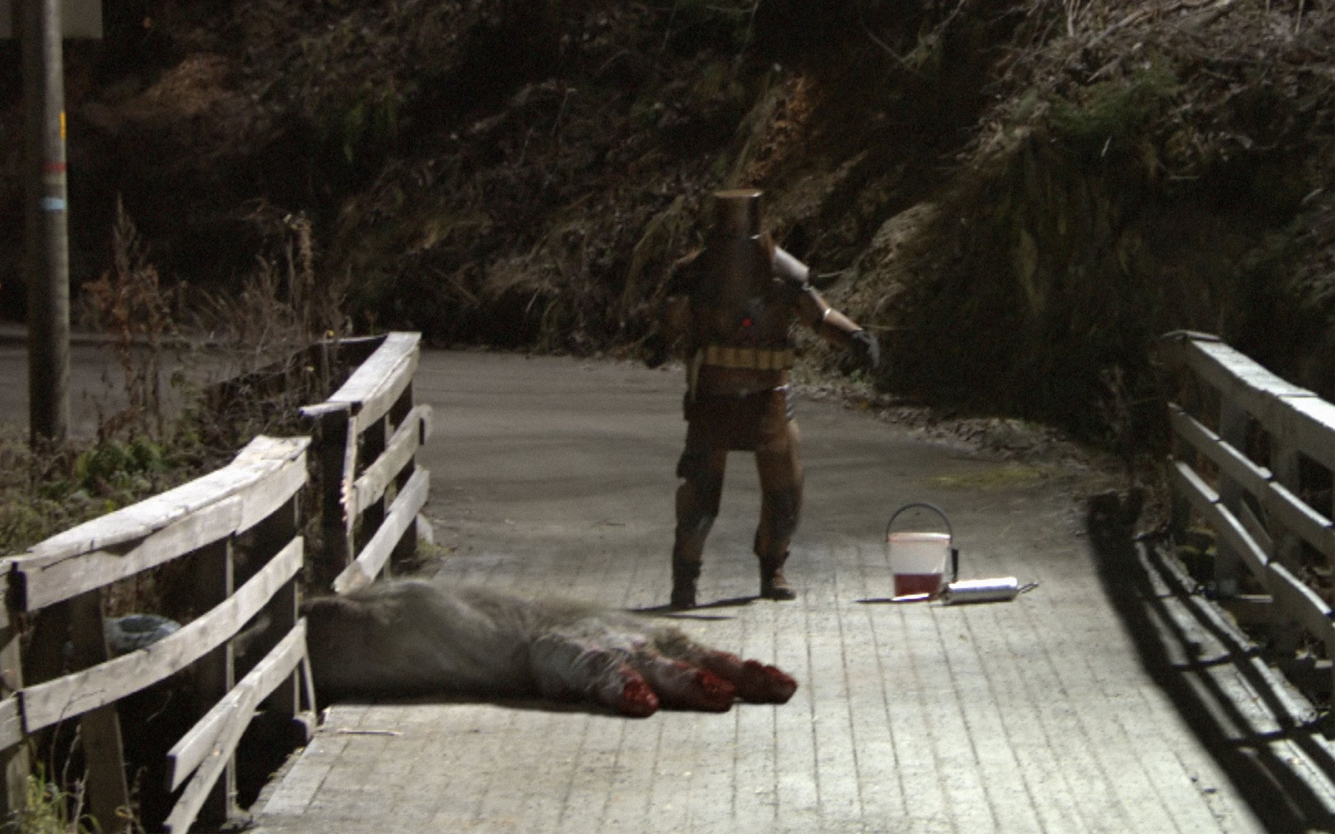 The Troll Hunter (movie) 2K Quad HD PC desktop wallpaper: a hunter on a wooden bridge stands beside a slain troll with massive bloodied feet, gear and a bloodied bucket nearby.
