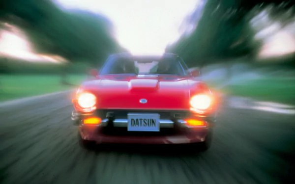 HD desktop wallpaper featuring a red Datsun vehicle captured with a motion blur effect on a road surrounded by greenery.