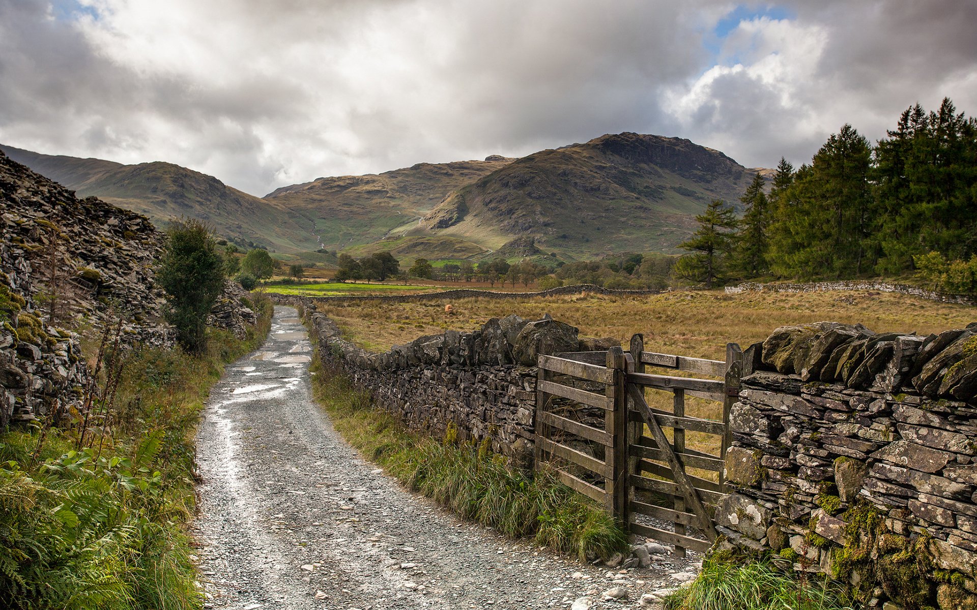 HD PC desktop wallpaper featuring a scenic nature path winding through stone walls and fields, set against a backdrop of rolling hills and a cloudy sky.