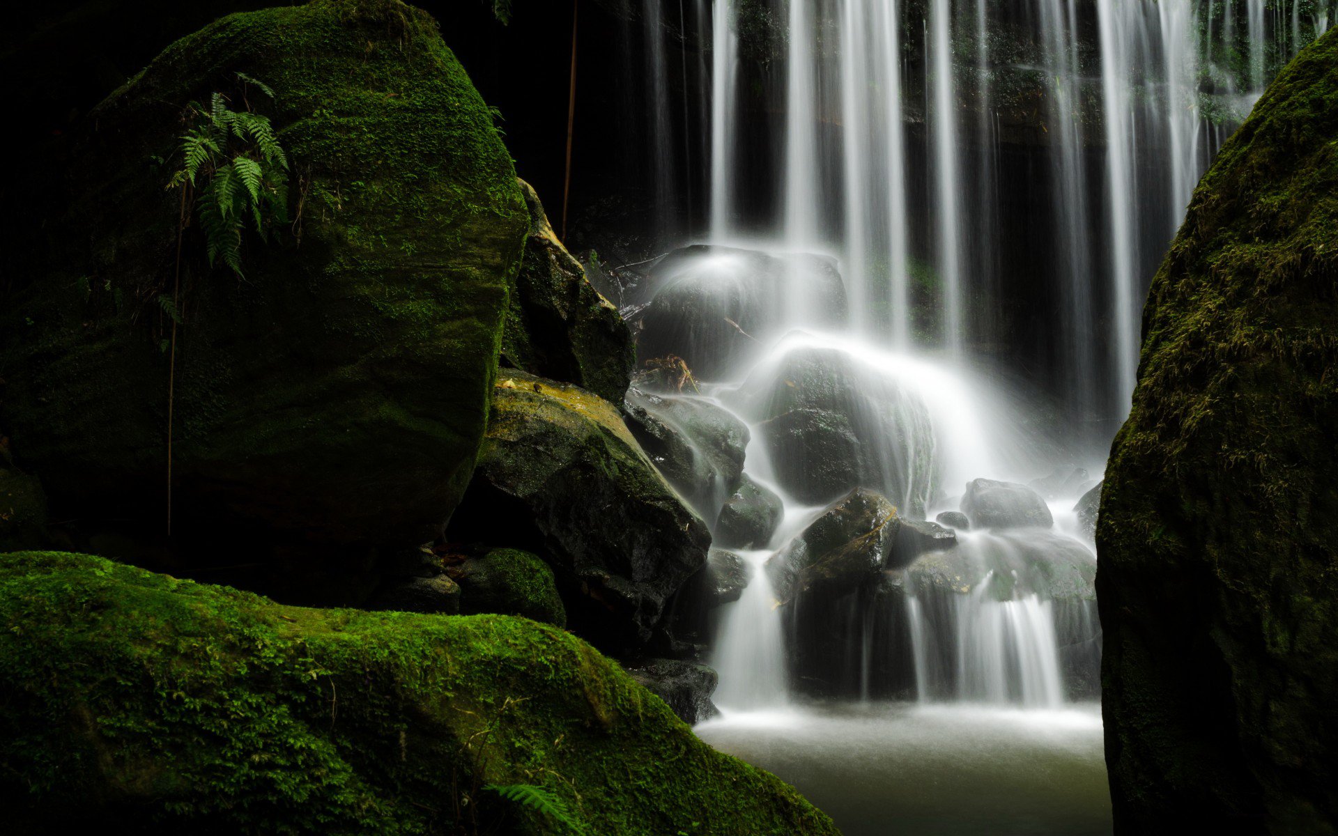 HD desktop wallpaper showcasing a serene waterfall cascading over moss-covered rocks in a lush, green natural setting.
