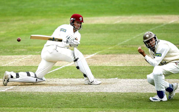 A cricketer plays a shot while another player prepares to catch the ball, set against a lush green field. HD desktop wallpaper background.