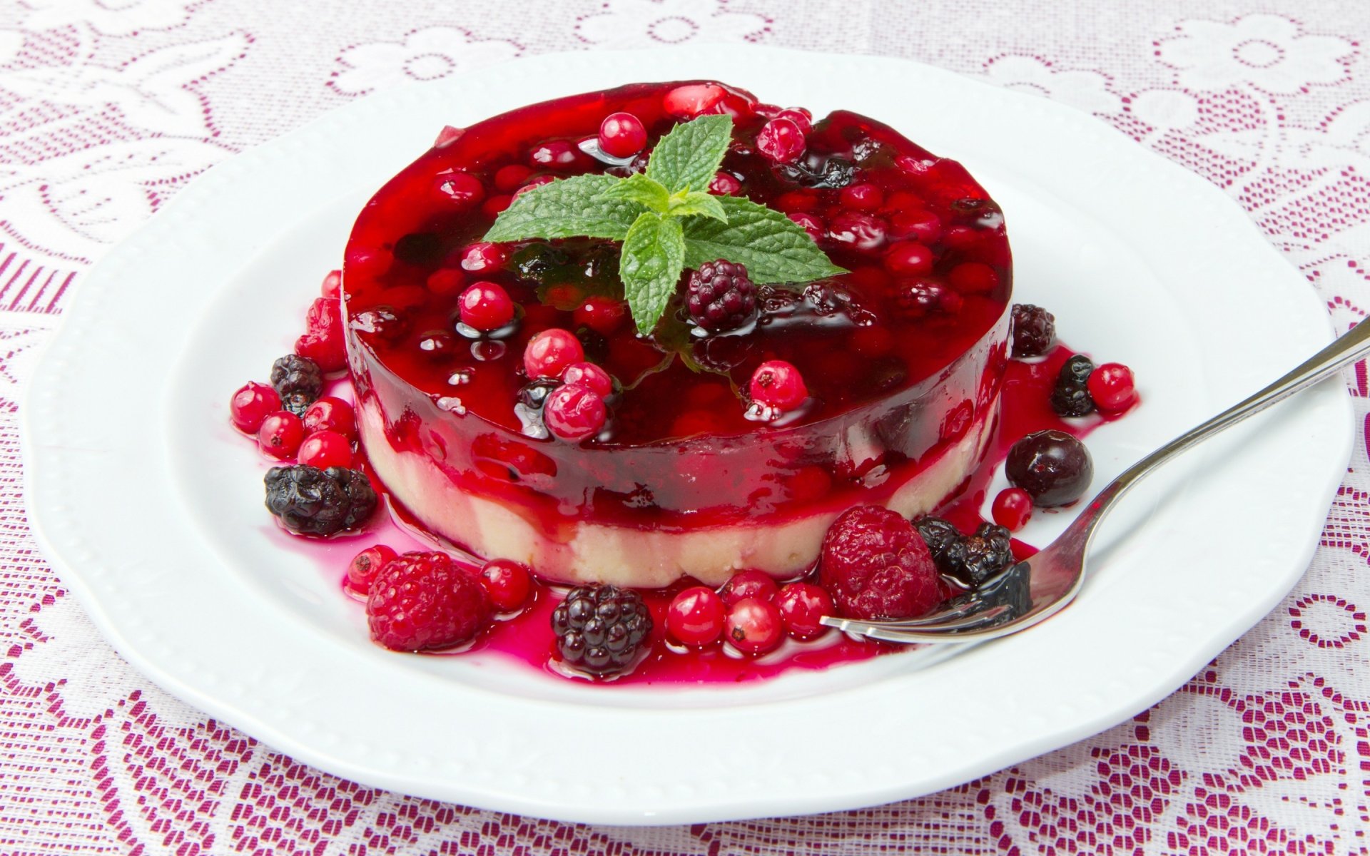 HD desktop wallpaper featuring a vibrant berry cake topped with a glossy red berry sauce and fresh mint, served on a white plate.