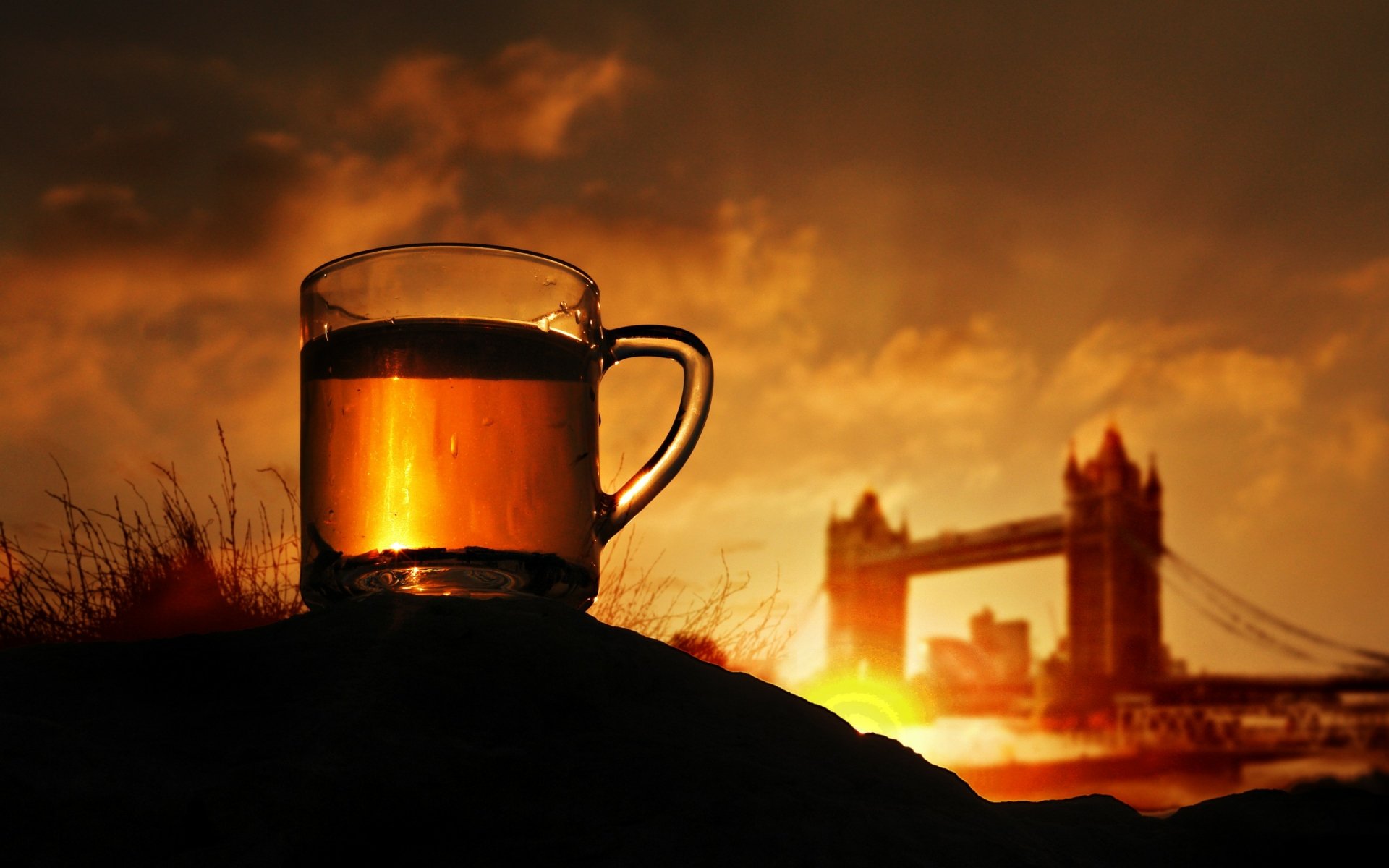 A glass of tea glows warmly in the foreground against a dramatic sunset backdrop featuring Tower Bridge, creating a serene and inviting HD desktop wallpaper.