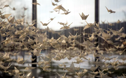 HD PC desktop wallpaper featuring numerous man-made origami cranes suspended in the air against a blurred outdoor background.