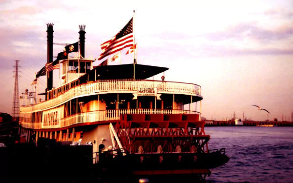 Paddle steamer boat (river vehicle) docked at dusk with American flag, multi‑deck silhouette over water — 2K Quad HD PC desktop wallpaper/background.