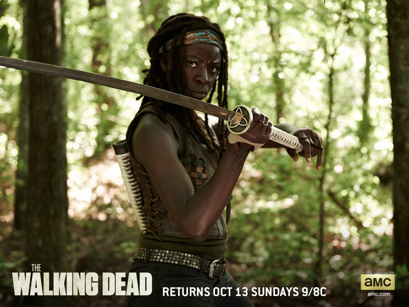 Danai Gurira as Michonne from The Walking Dead wields a katana in this striking HD wallpaper, set in a lush forest backdrop. A true homage to the iconic character.