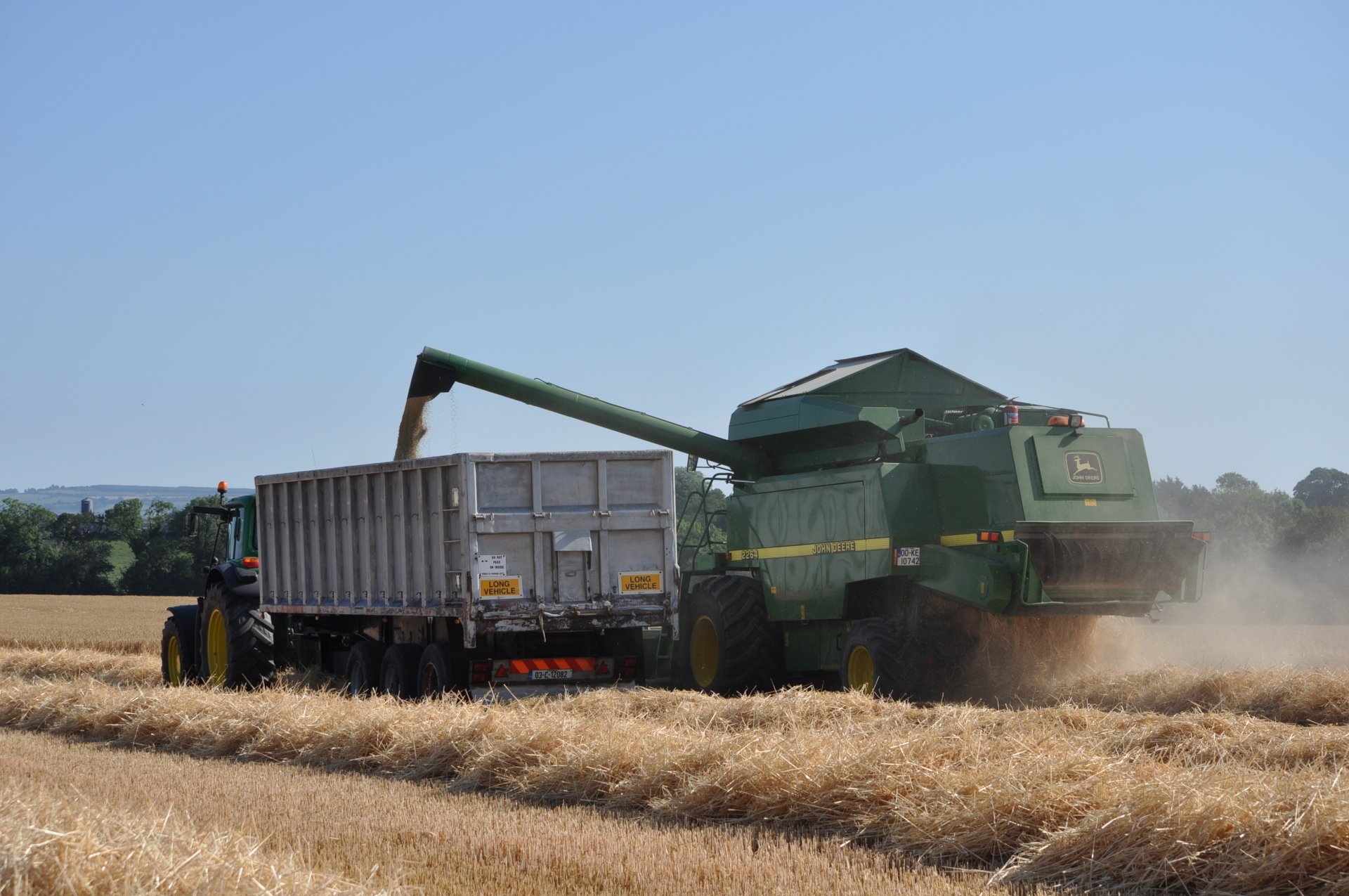 HD PC desktop wallpaper showing a John Deere vehicle harvesting crops in a golden field under a clear blue sky.