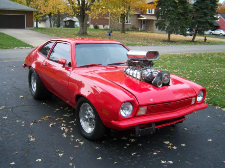 HD desktop wallpaper featuring a bright red Ford Pinto with a prominent supercharged engine parked on a driveway in a suburban neighborhood.