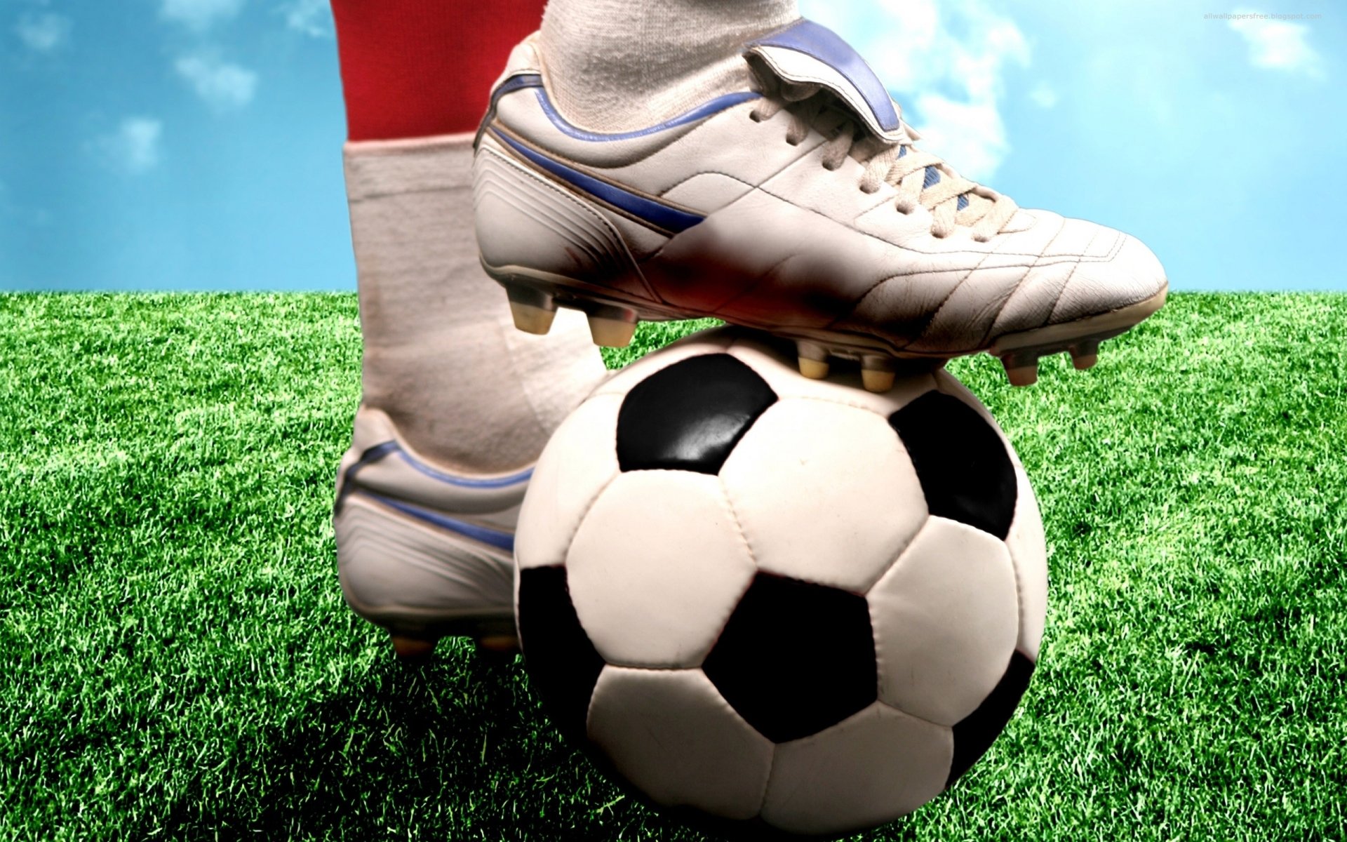 HD PC desktop wallpaper showcasing a close-up of a soccer player's foot in cleats resting on a classic black and white soccer ball on vibrant green grass under a blue sky.