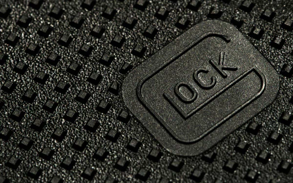 Close-up view of a textured Glock pistol grip with the embossed Glock logo. This HD desktop wallpaper showcases fine details of the man-made firearm component.