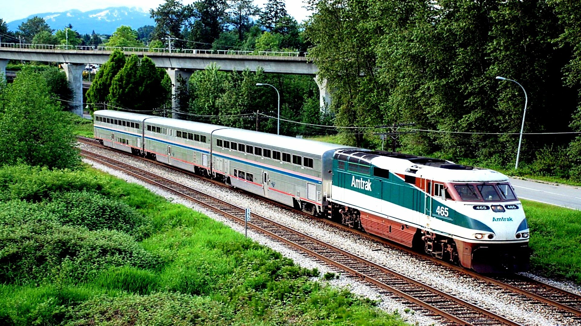 HD PC desktop wallpaper featuring a train traveling along tracks surrounded by greenery and a nearby bridge under a clear blue sky.