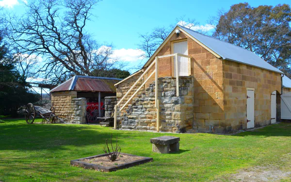 HD desktop wallpaper of Eskbank House in Lithgow, Australia, featuring a historic stone building, cart, and bare tree branches under a clear blue sky.