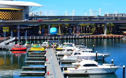 HD desktop wallpaper of Sydney’s Darling Harbour marina in Australia, featuring yachts docked by a pier near a highway and taxi stand along the harbor’s waterfront.