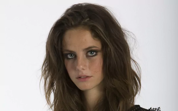A striking HD wallpaper featuring actress Kaya Scodelario, highlighting her captivating gaze and tousled hair against a simple backdrop.