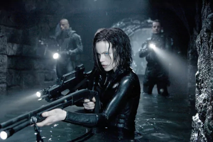 HD wallpaper featuring Kate Beckinsale in Underworld: Evolution, armed and poised in a dark, water-filled setting, flanked by armed companions. A striking cinematic moment.