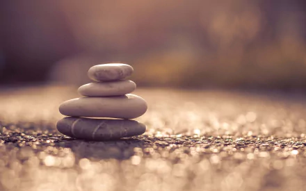 HD PC desktop wallpaper: nature scene with a small stack of smooth stones on a sunlit pebbled surface and a warm, blurred bokeh background.