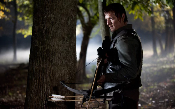 Daryl Dixon, portrayed by Norman Reedus, stands against a tree with a bow in hand, set in a misty forest backdrop from the TV show The Walking Dead. HD wallpaper showcasing intense survival.