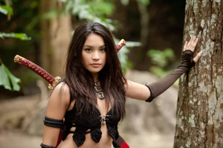 A character from The Scorpion King 3: Battle for Redemption poses confidently against a tree, showcasing a fierce expression and intricate costume details. An engaging HD desktop wallpaper.