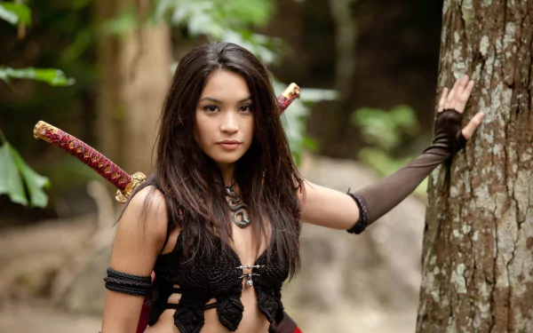 A character from The Scorpion King 3: Battle for Redemption poses confidently against a tree, showcasing a fierce expression and intricate costume details. An engaging HD desktop wallpaper.