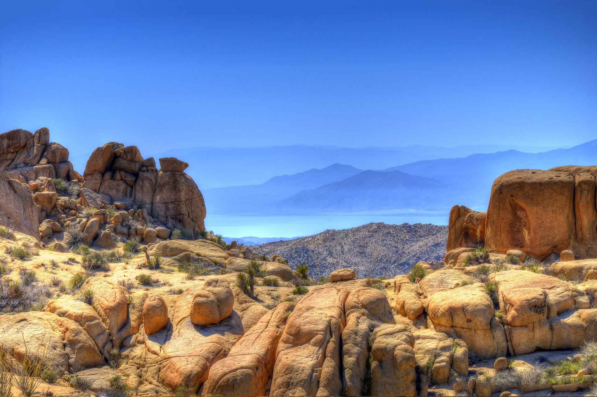 4K Ultra HD PC desktop wallpaper of sunlit rock formations and boulders in a desert valley with hazy blue mountains and a clear sky — nature, rock.