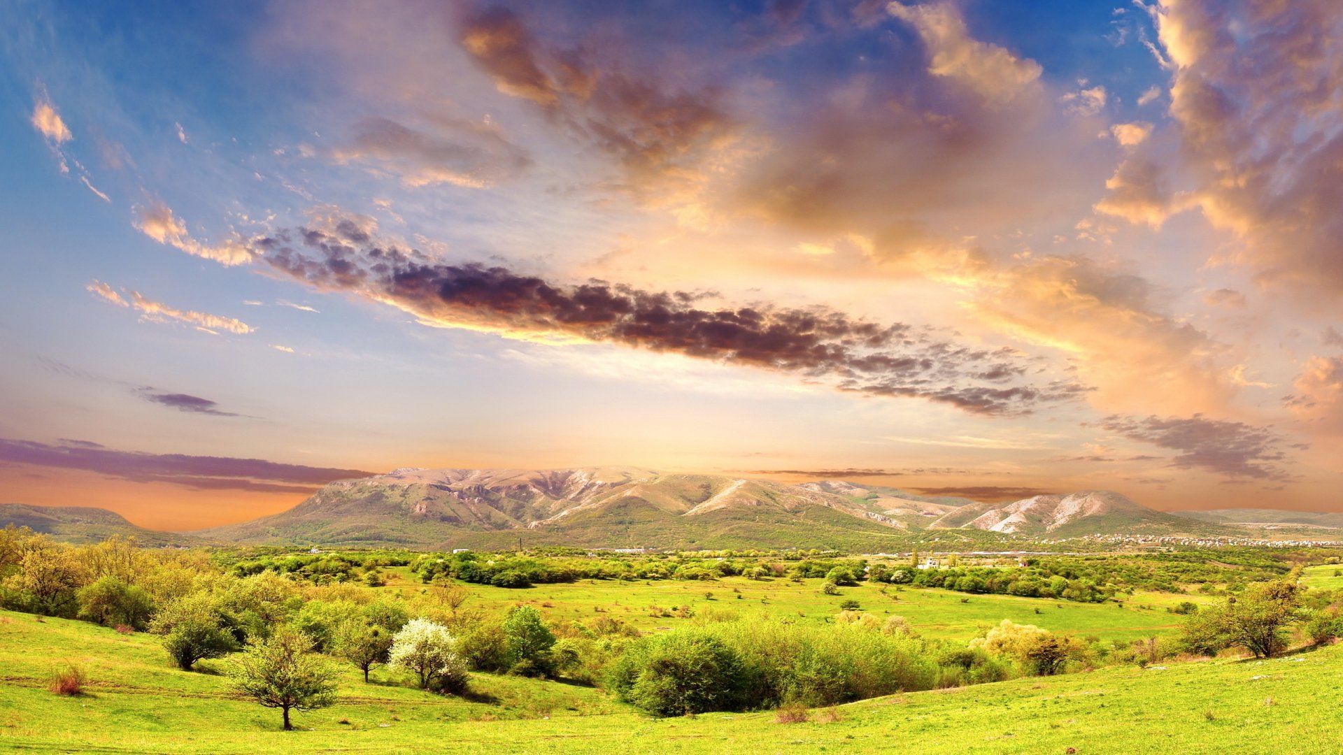 HDR nature landscape featuring a green field with scattered trees under a dramatic, colorful sky, captured as a high-definition PC desktop wallpaper and background.