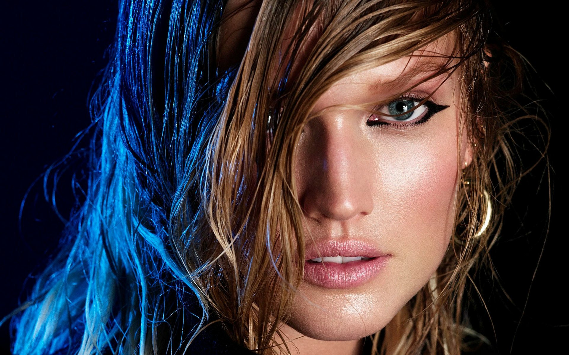 Close-up of a woman's face with striking features and dramatic makeup, set against a dark background. This HD image serves as a captivating desktop wallpaper.