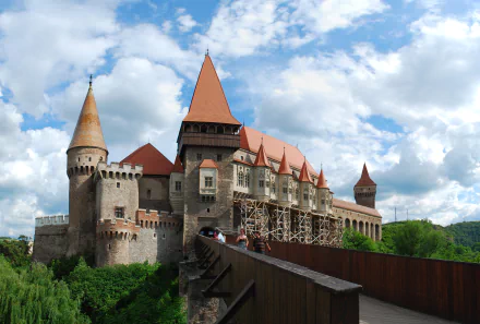 4K Ultra HD wallpaper of the man-made Corvin Castle with its distinctive red roofs and towers set against a partly cloudy blue sky backdrop.