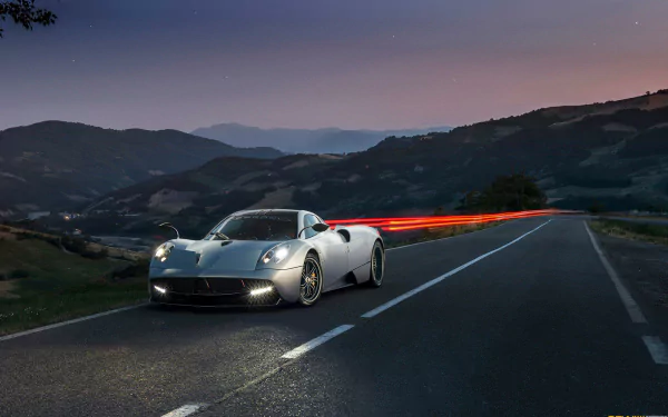 A striking Pagani Huayra positioned on a winding road, capturing motion with light trails against a twilight mountain backdrop. An HD desktop wallpaper that emphasizes automotive elegance.